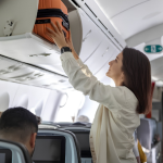 Passenger placing a cabin bag in an aircraft overhead bin during boarding.