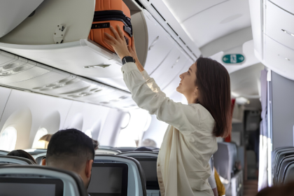 Passenger placing a cabin bag in an aircraft overhead bin during boarding.
